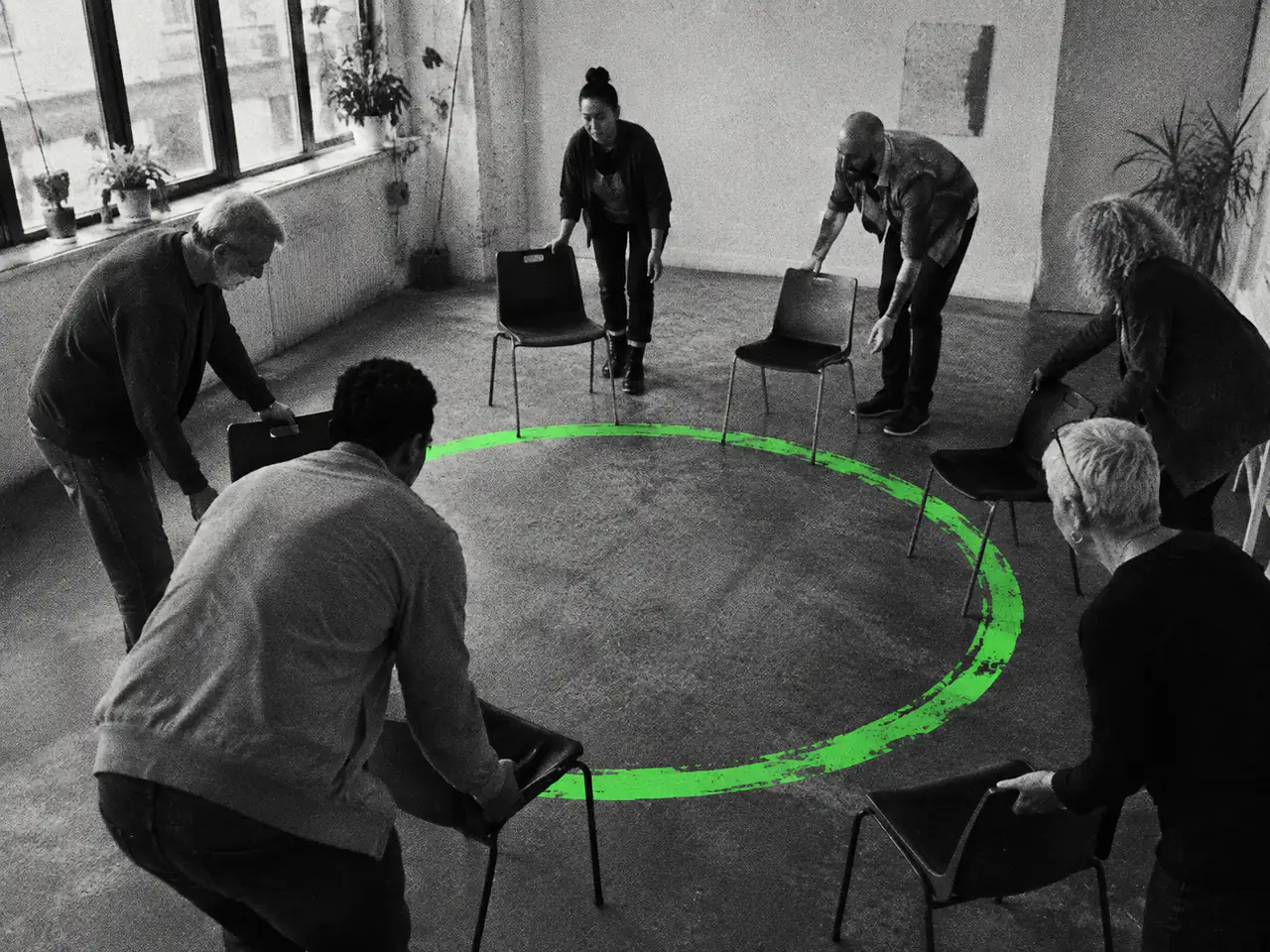 People arrange chairs around a green circle on the floor.
